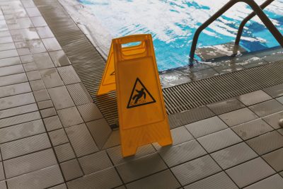 A caution wet floor sign placed near a swimming pool to ensure safety around the slippery area. Un panneau d'avertissement de sol mouillé placé près d'une piscine pour assurer la sécurité autour de la zone glissante.