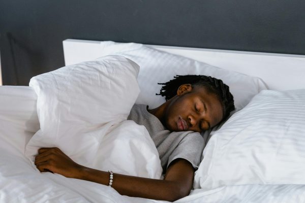 An adult sleeping peacefully on a bed with white pillows and linen. Un adulte dormant paisiblement sur un lit avec des oreillers et du linge blanc.