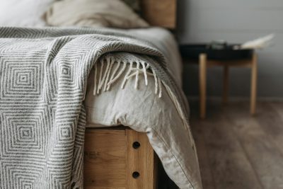 A cozy bedroom with a wooden bed, pillows, and a patterned blanket on a wooden floor. Une chambre confortable avec un lit en bois, des oreillers et une couverture à motifs sur un plancher en bois.