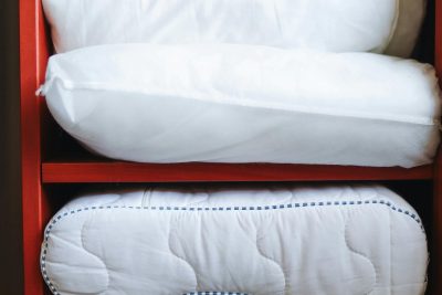 A hand adjusting pillows on a neatly organized red shelf, emphasizing home tidiness. Une main ajustant des oreillers sur une étagère rouge bien organisée, soulignant la propreté de la maison.