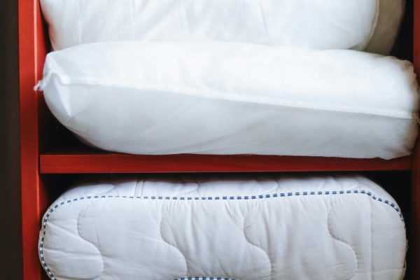 A hand adjusting pillows on a neatly organized red shelf, emphasizing home tidiness. Une main ajustant des oreillers sur une étagère rouge bien organisée, soulignant la propreté de la maison.