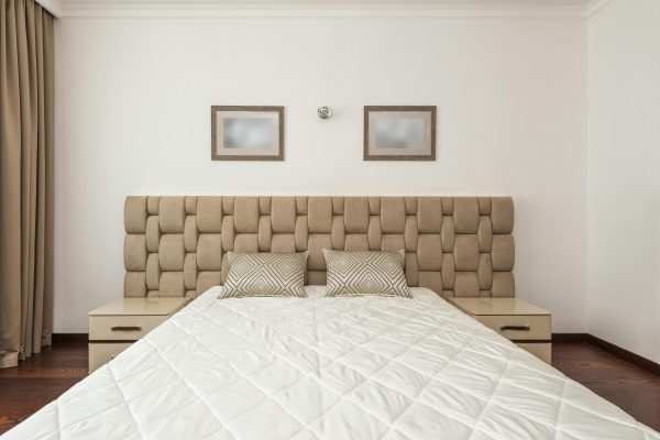 Elegant beige bedroom featuring a quilted headboard, plush pillows, and minimalistic decor. Chambre élégante beige avec une tête de lit matelassée, des oreillers moelleux et une décoration minimaliste.