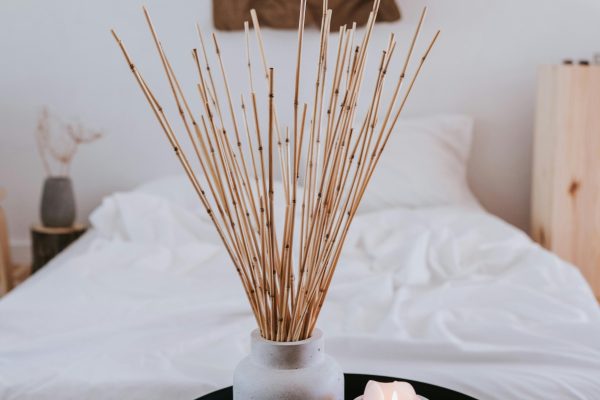 A minimalist bedroom featuring a candle, vase with sticks, and a cozy ambiance. Une chambre minimaliste avec une bougie, un vase avec des bâtons et une ambiance confortable.