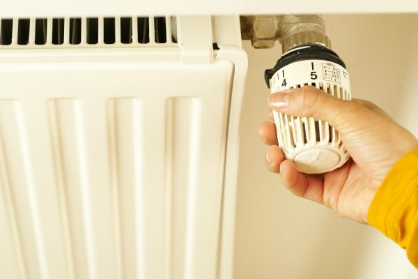 Close-up of hand adjusting radiator thermostat to control home heating temperature. Gros plan sur une main ajustant le thermostat du radiateur pour contrôler la température de chauffage de la maison.