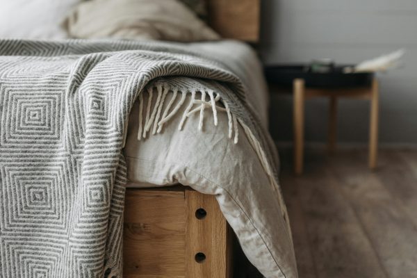 A cozy bedroom with a wooden bed, pillows, and a patterned blanket on a wooden floor. Une chambre douillette avec un lit en bois, des oreillers et une couverture à motifs sur un plancher en bois.