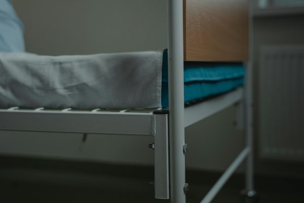 Close-up view of a hospital bed with white linens and metal frame, indoors. Vue rapprochée d'un lit d'hôpital avec du linge blanc et un cadre métallique, à l'intérieur.