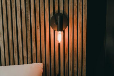 Warm bedroom interior featuring a glowing Edison bulb on a wooden slat wall, creating a cozy atmosphere. Intérieur de chambre chaleureuse avec une ampoule Edison brillante sur un mur à lattes en bois, créant une atmosphère confortable.