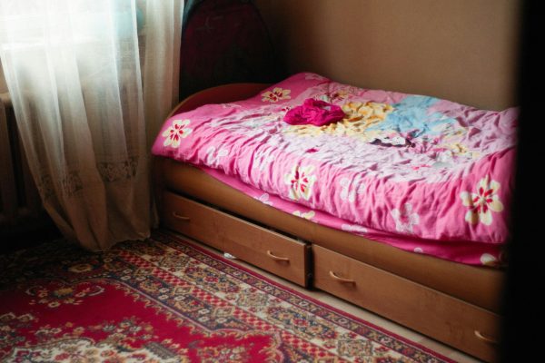 A warm and inviting bedroom scene featuring a floral pink bedspread, under-bed drawers, and a patterned rug. Une chambre à coucher chaleureuse et accueillante avec un couvre-lit rose à motifs floraux, des tiroirs sous le lit et un tapis à motifs.