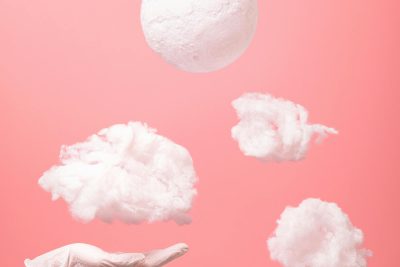 An artistic composition of floating clouds and hand with medical glove against a pink backdrop. Une composition artistique de nuages flottants et d'une main avec un gant médical sur un fond rose.