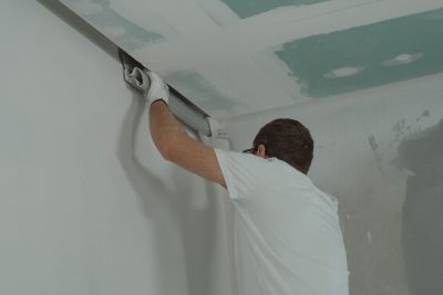 A man works meticulously on drywall installation during a house renovation. Un homme travaille méticuleusement à l'installation de plaques de plâtre lors d'une rénovation domiciliaire.