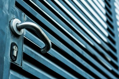 Close-up of a sleek stainless steel door handle and lock on a blue metallic door. Gros plan sur une poignée de porte en acier inoxydable lisse et un verrou sur une porte métallique bleue.