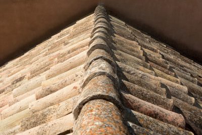 Close-up shot of vintage clay roof tiles with visible moss, showcasing texture and age. Gros plan de tuiles de toit en argile vintage avec mousse visible, mettant en évidence la texture et l'âge.