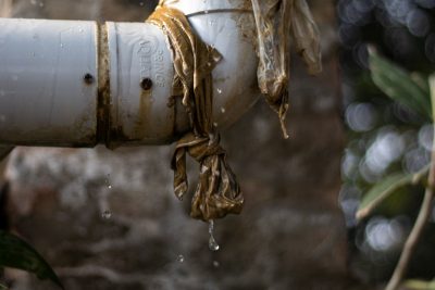 Close-up of a leaking plastic pipe outdoors with water dripping, showing wear and tear. Gros plan d'un tuyau en plastique qui fuit à l'extérieur avec de l'eau qui goutte, montrant l'usure.