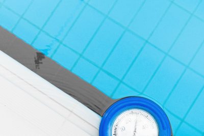 A clear swimming pool with a thermometer measuring water temperature. Top view shot. Une piscine cristalline avec un thermomètre mesurant la température de l'eau. Vue de dessus.