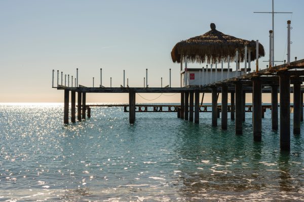 A peaceful view of a rustic ocean pier with a traditional hut during sunrise reflecting light on the water. Une vue paisible d'une jetée océanique rustique avec une hutte traditionnelle au lever du soleil reflétant la lumière sur l'eau.