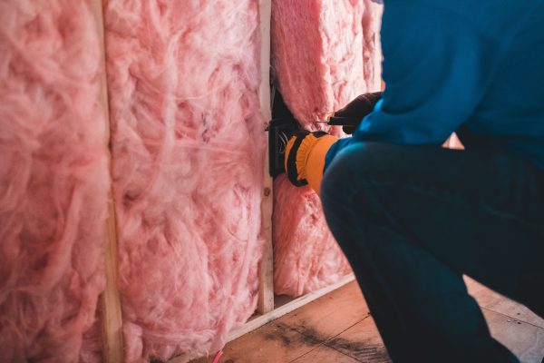 Crop unrecognizable worker in gloves sitting on haunches and insulating with pink stone wool Ouvrier non identifiable en gants accroupi et isolant avec de la laine de pierre rose