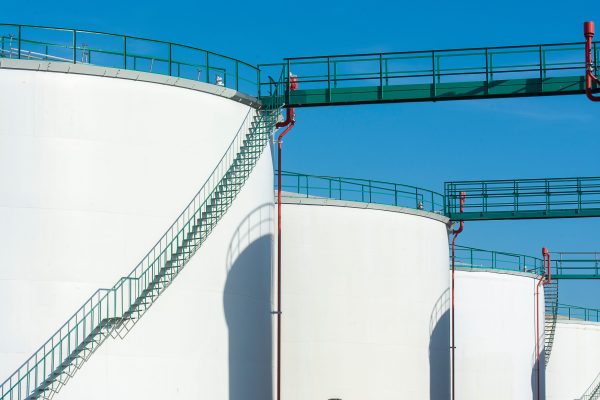 Large industrial storage tanks with a green walkway under a clear blue sky. Grands réservoirs de stockage industriels avec une passerelle verte sous un ciel bleu clair.